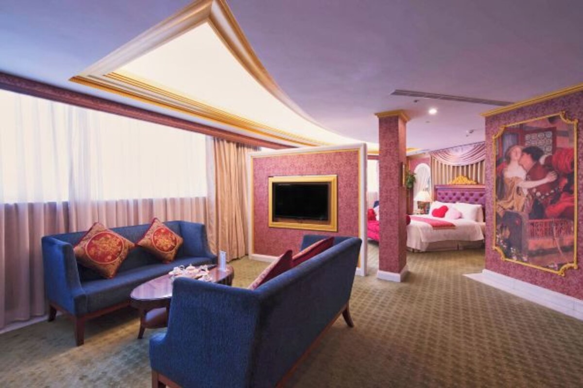 Habitación de hotel con sala de estar que incluye un sofá, sillones, un televisor y una cama con cabecera roja.