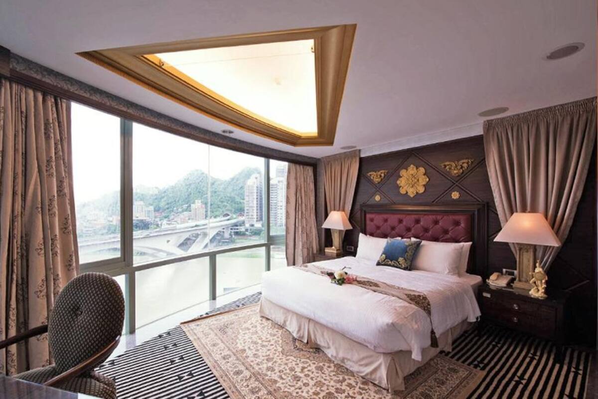 A hotel room with a large bed, a view of a cityscape, and a modern ceiling design.