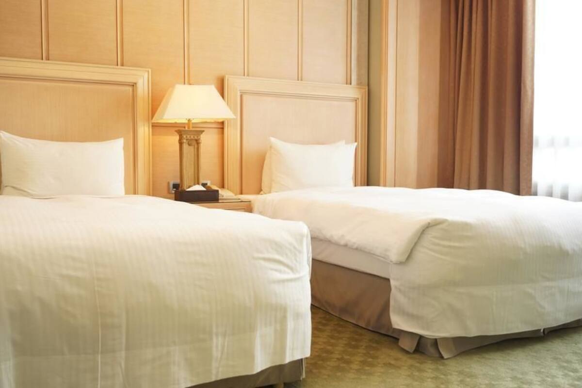 Una habitación de hotel con dos camas, una mesita de noche con lámpara y una ventana con cortinas.