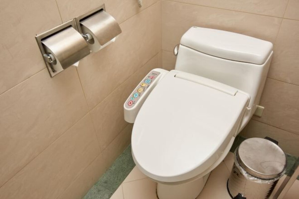 Un inodoro moderno con panel de control digital, dispensador de papel higiénico y un cubo de basura.