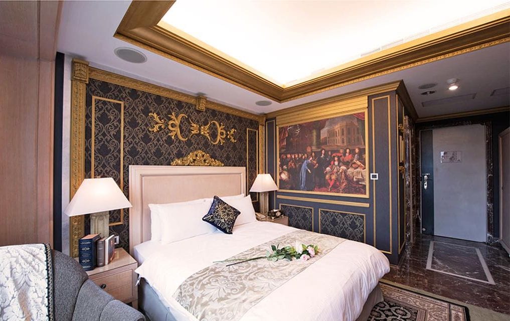 A hotel room with a large bed, two bedside lamps, a decorative headboard, and a wall mural.