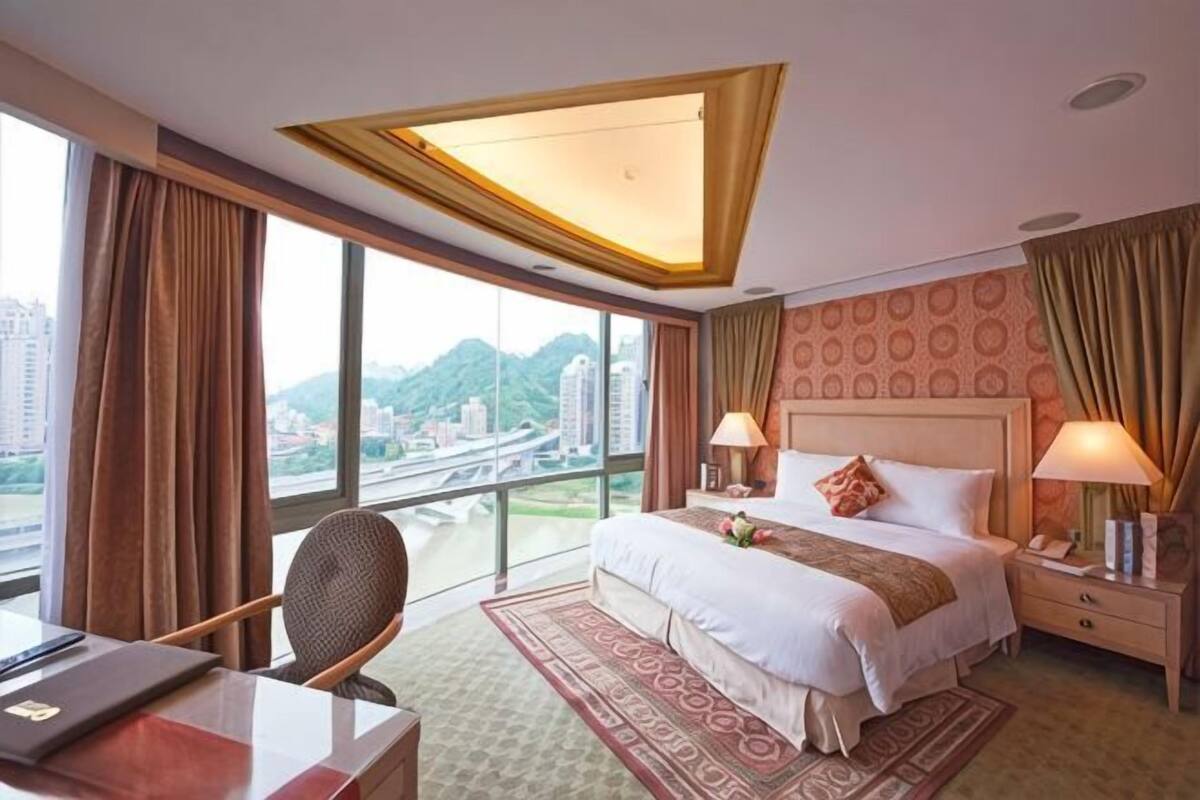 A hotel room with a large bed, two bedside tables, a desk, and a chair.