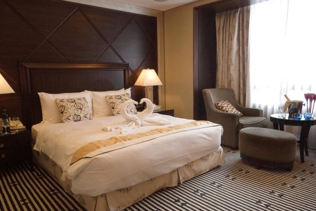 Una habitación de hotel con una cama grande, una silla, una mesita y una ventana con cortinas.