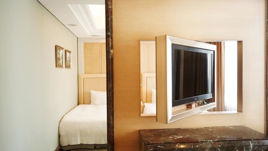 Habitació d'hotel amb llit, televisió penjada a la paret i un aparador de fusta.