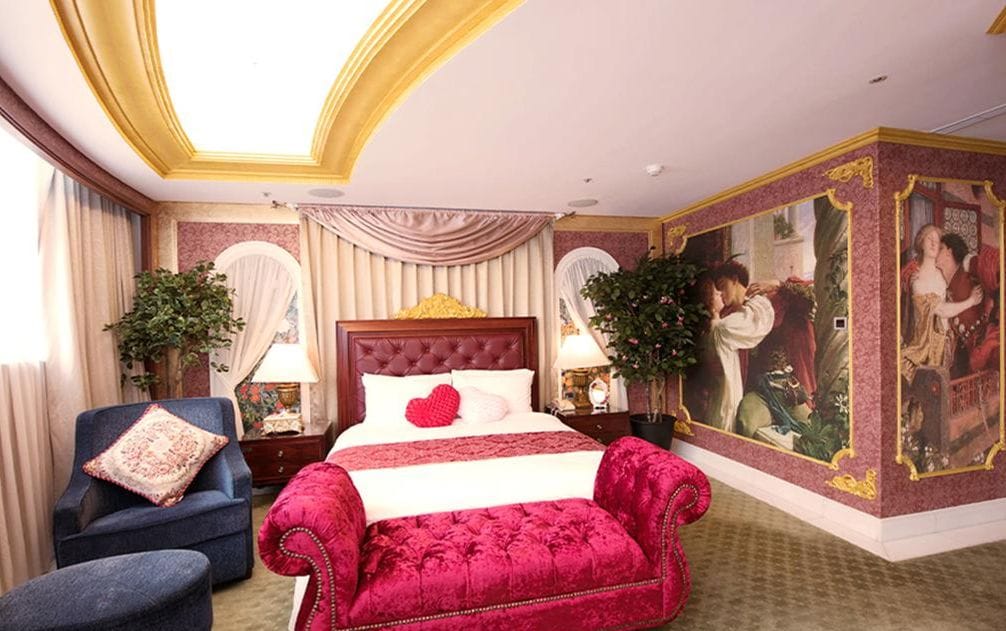 Un dormitori luxós amb un llit gran, una cadira tapissada de color vermell i un quadre clàssic a la paret.