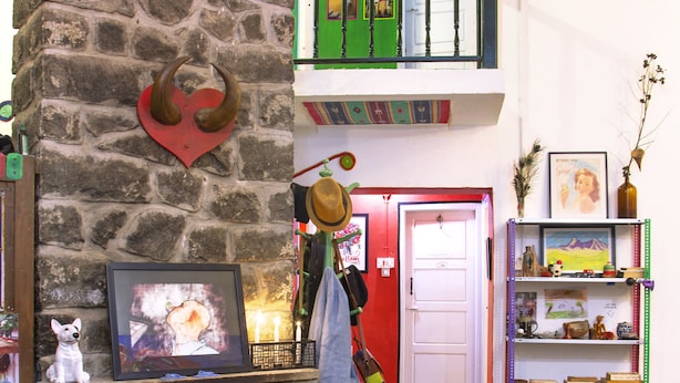 Ein gemütliches Interieur mit Kamin aus Stein, einer Hundefigur, einem farbenfrohen Teppich und einer Farbgestaltung in Grün und Weiß.