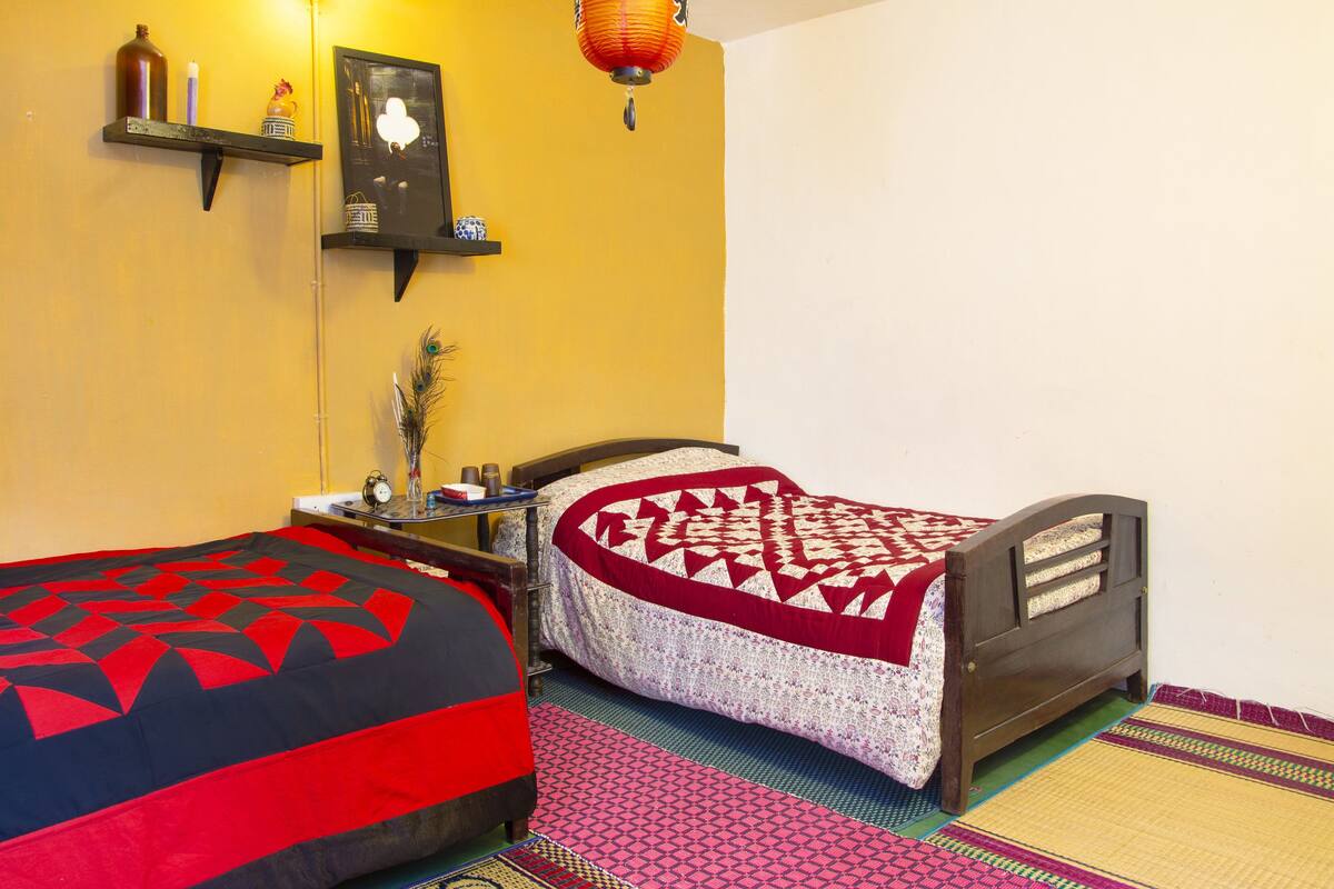 Una habitación con dos camas, una mesita de noche, una estantería decorada y un reloj en la pared.