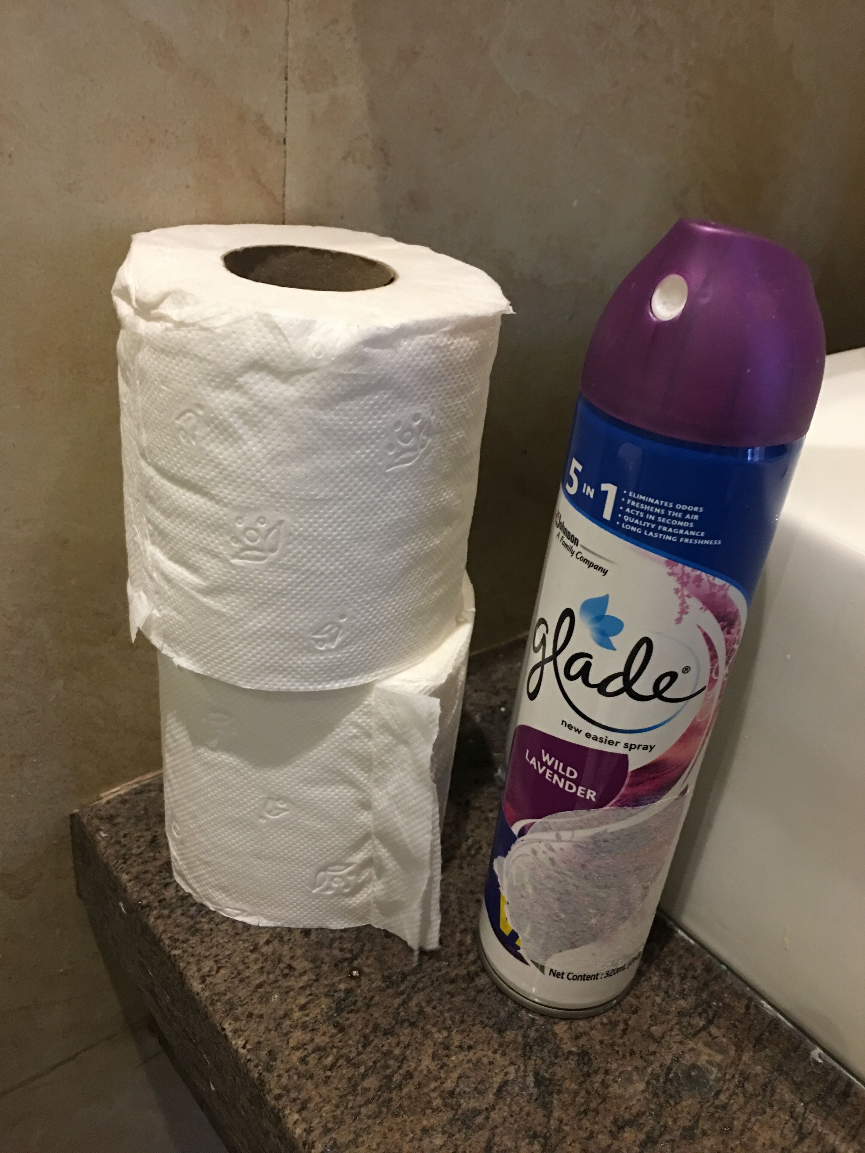 Un rotllo de paper higiènic i una llauna de perfum ambient Glade sobre un taulell de granat.