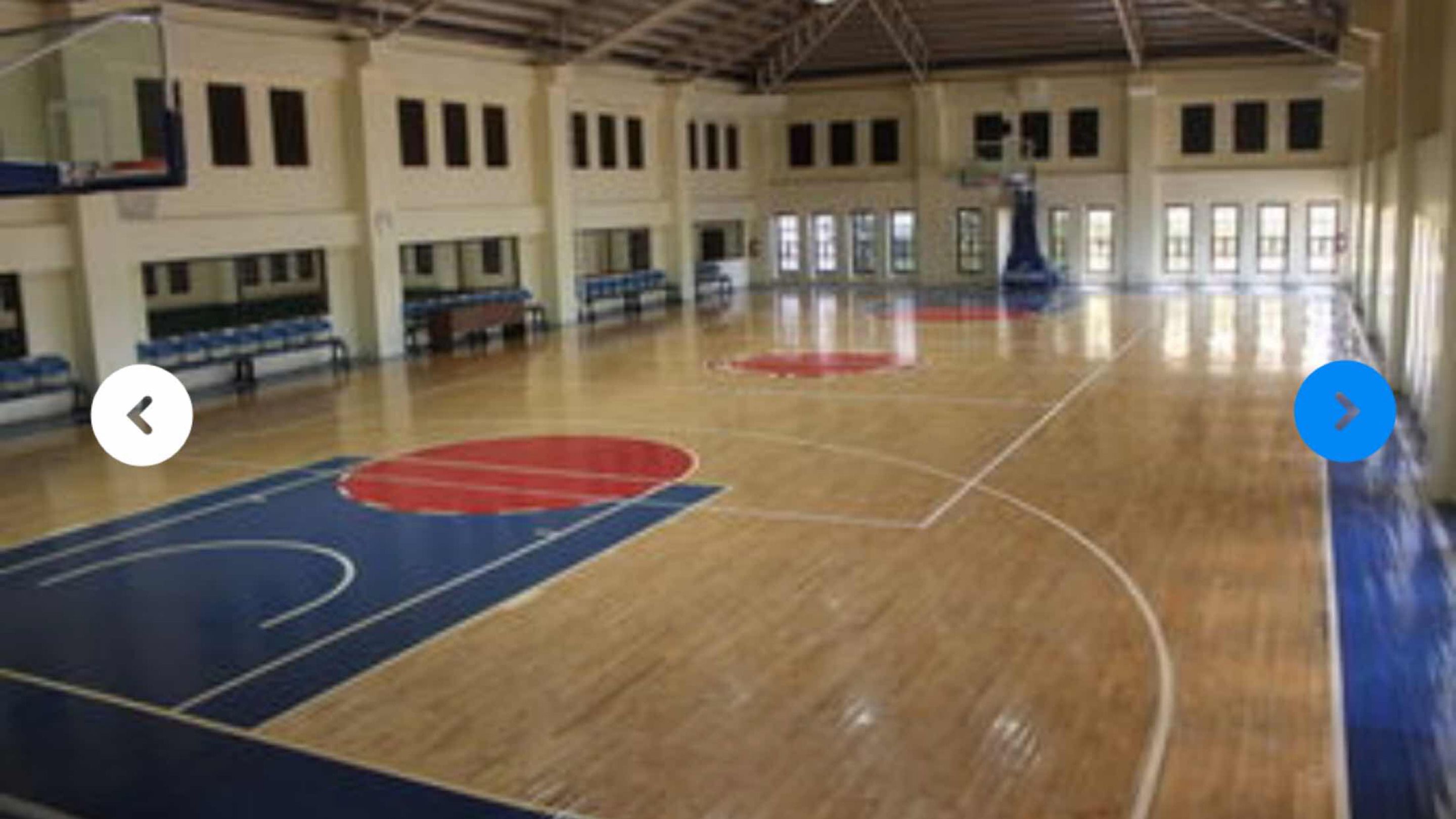 Eine Sporthalle mit einer Holzbodenfläche, einem Basketballkorb und einer Sitzgelegenheit mit Bänken.