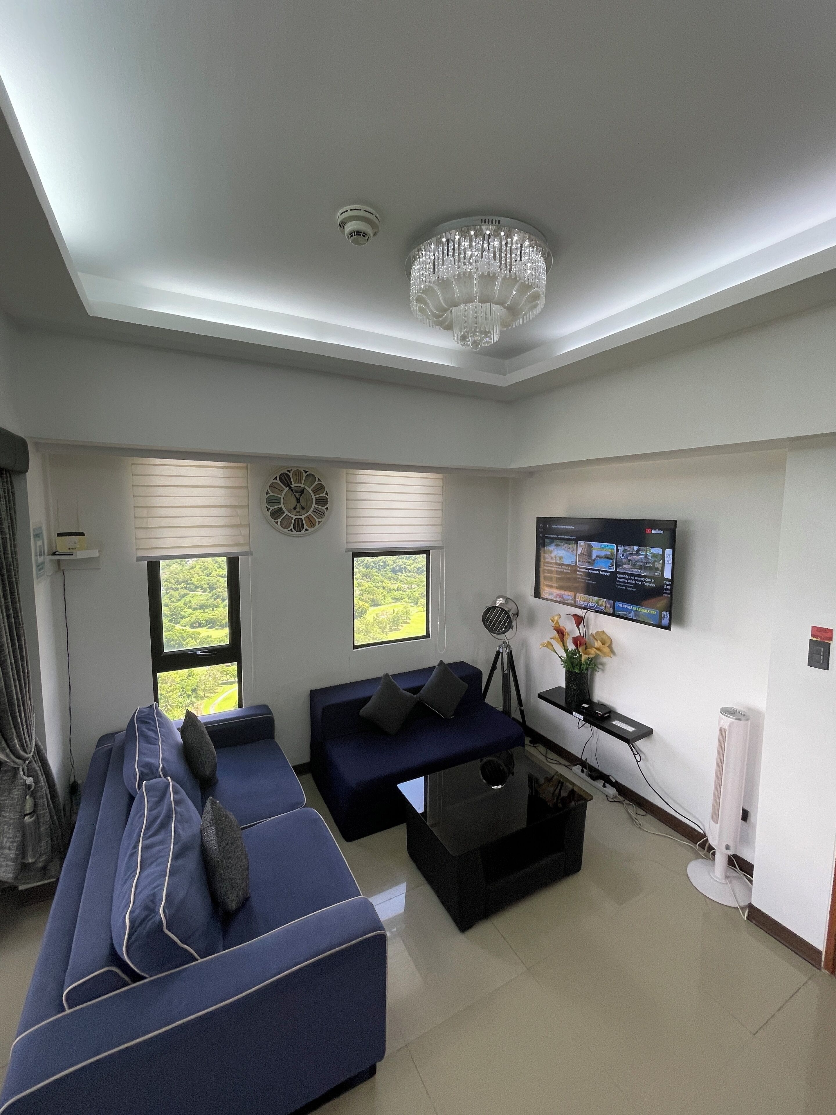 Una sala de estar moderna con un sofá azul, una mesita de centro negra, una lámpara de pie, un televisor montado en la pared y un candelabro.