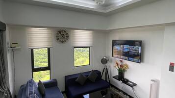 Una sala de estar moderna con un sofá azul, una mesita de centro negra, una lámpara de pie, un televisor montado en la pared y un candelabro.