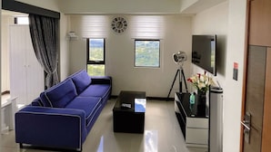 A modern living room with a blue sofa, a coffee table, a TV, and a chandelier. - Splendido Tower 2 Ann's Unit  (Laurel)