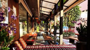 A covered outdoor seating area with wooden benches and cushions, surrounded by potted plants and flowers. - Panda House Chiang Mai (Chiang Mai)