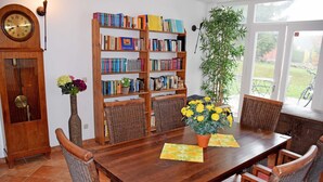 A dining area with a wooden table, wicker chairs, a bookshelf, and a clock on the wall. - 08 Apartment (H) - Apartments in Ostseebad Göhren REB785 (Göhren)
