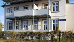 A two-story building with a balcony on the upper floor, a sign reading "Alte Kirchstraße," and a fence with greenery in front. - 08 Apartment (H) - Apartments in Ostseebad Göhren REB785 (Göhren)