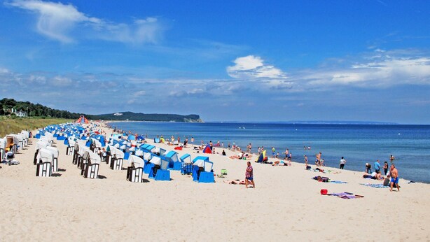 A beach with rows of blue and white beach chairs and umbrellas, a sandy shore, and the sea in the background. - 08 Apartment (H) - Apartments in Ostseebad Göhren REB785 (Göhren)