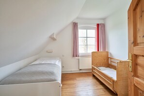 Une petite pièce bien éclairée, avec un lit simple, un banc en bois et une armoire.
