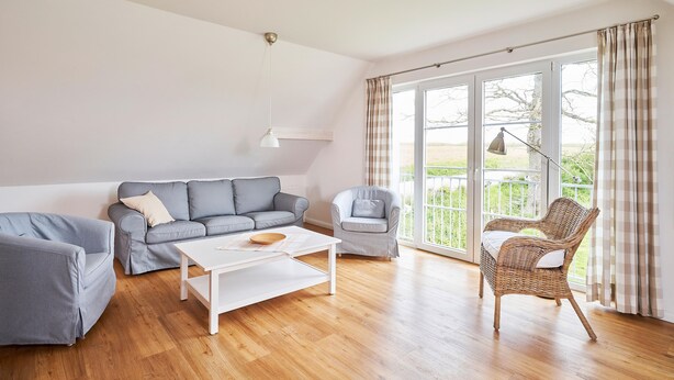 Ein Wohnzimmer mit einer Couch, Sesseln, einem Couchtisch und einem Korbstuhl.