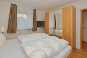 Ein Hotelzimmer mit einem großen Bett, einem Fernseher, einem Kleiderschrank und einem Vorhangfenster.