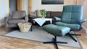 A living room with a brown leather sofa, a green armchair, a small table with a vase of red tulips, and a painting of a beach scene on the wall. - N 6 (BC.a5) - Stranddomicil Steiner (Büsum)