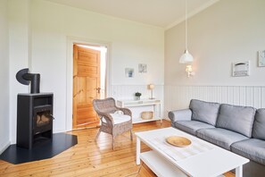 A cozy living room with a black wood-burning stove, a grey sofa, a wicker chair, and a white coffee table.