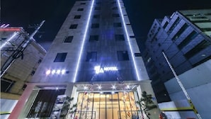 Un hotel con un llamativo letrero que dice 'HOTEL' en la entrada, una fachada moderna y una estructura alta con ventanas iluminadas.