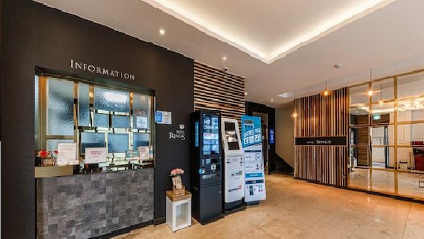 Un área de recepción de hotel con diseño moderno, que incluye un mostrador de recepción, mostradores de información y quioscos de autoservicio.