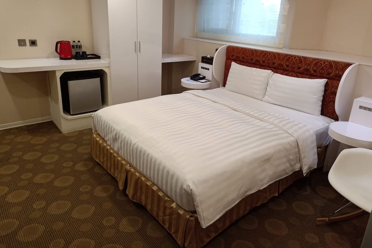Een hotelkamer met een bed, een bureau, een stoel, een bijzettafeltje, een raam en een kledingkast.