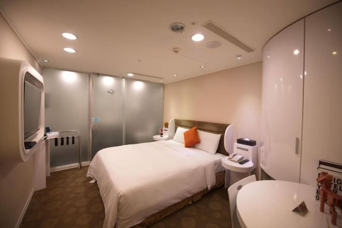 A hotel room with a bed, bedside table, nightstand, and a large wardrobe.