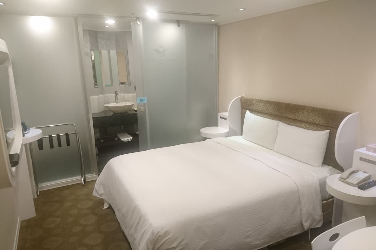 Hotelkamer met een bed, nachtkastje met telefoon en zakdoekjes, badkamer met wastafel en toilet, en een douchehoek.