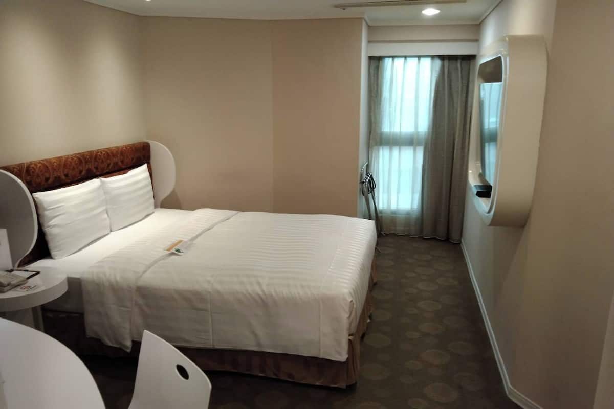 Een hotelkamer met een bed, een ronde tafel, een stoel, een spiegel en een raam met gordijnen.
