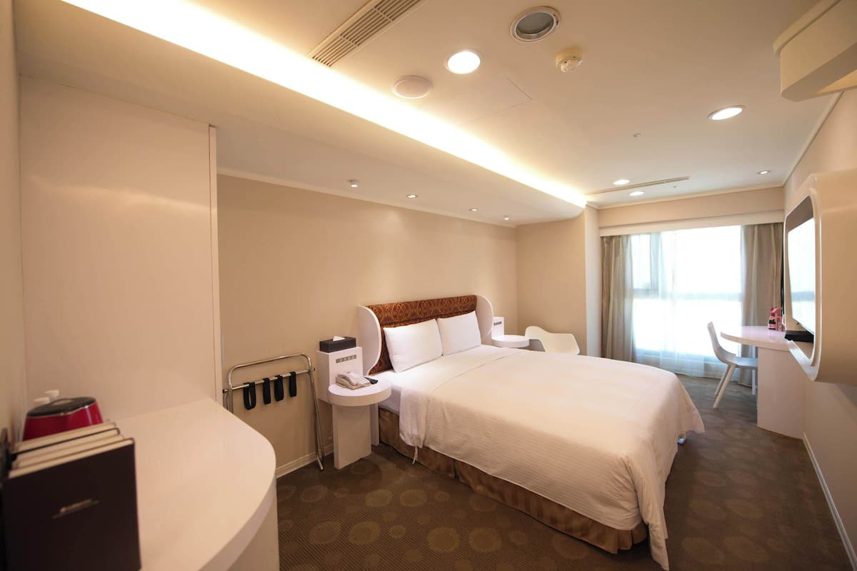 Een hotelkamer met een groot bed, nachtkastjes, een bureau en een raam met gordijnen.