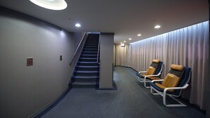 A hallway with a staircase, a waiting area with chairs, and a curtain-covered wall. - Ximen Airline Hotel (Taipei)