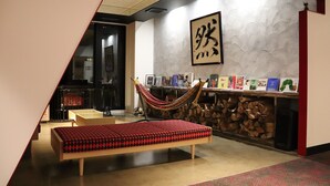 A room with a hammock, a bed, a bookshelf with books, and a wall with calligraphy. - Hotel Rosso Karuizawa (Karuizawa)