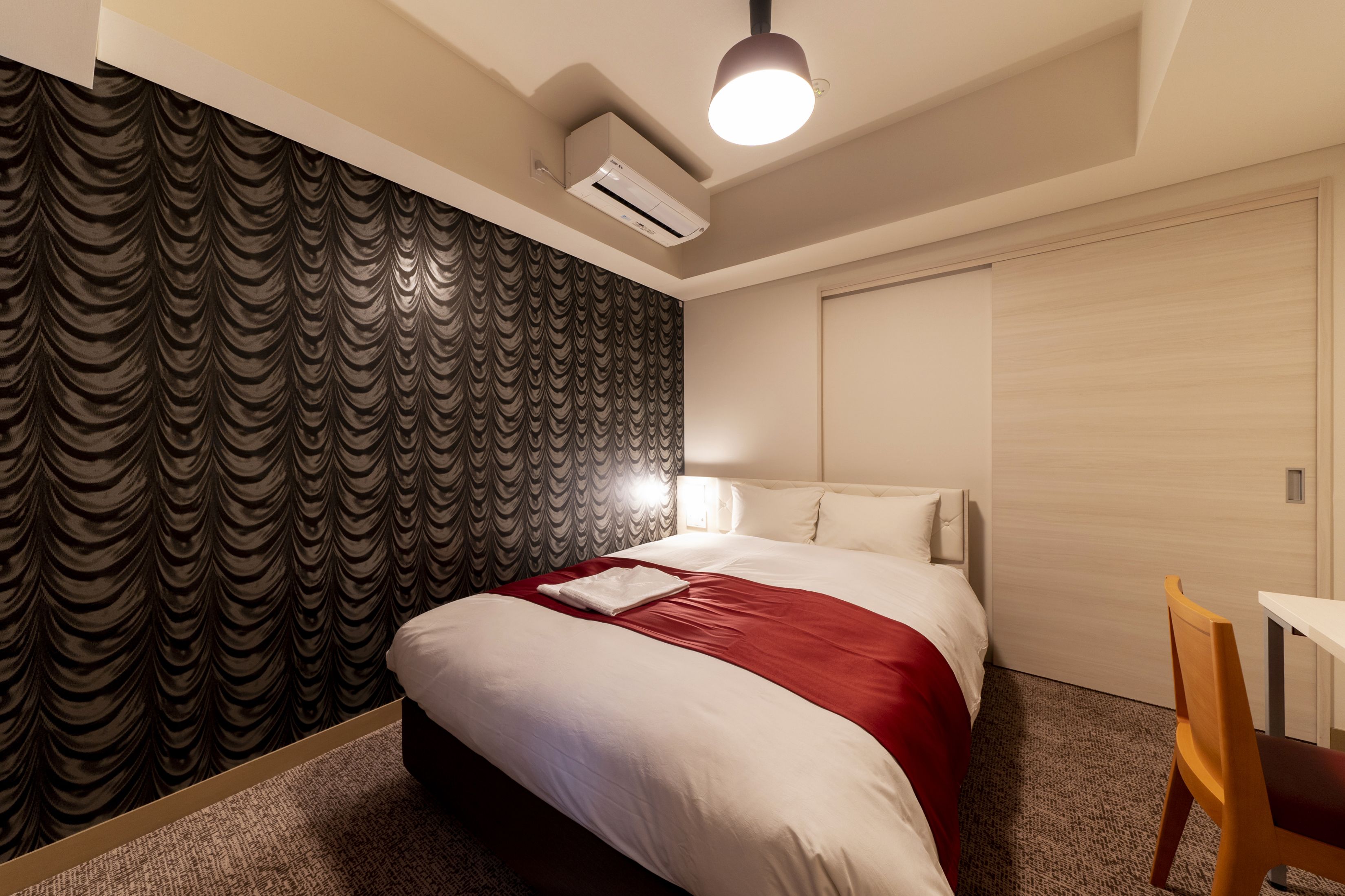 Quarto de hotel com cama, escrivaninha e ar condicionado na parede.