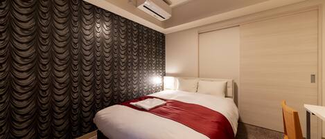 Quarto de hotel com cama, escrivaninha e ar condicionado na parede.