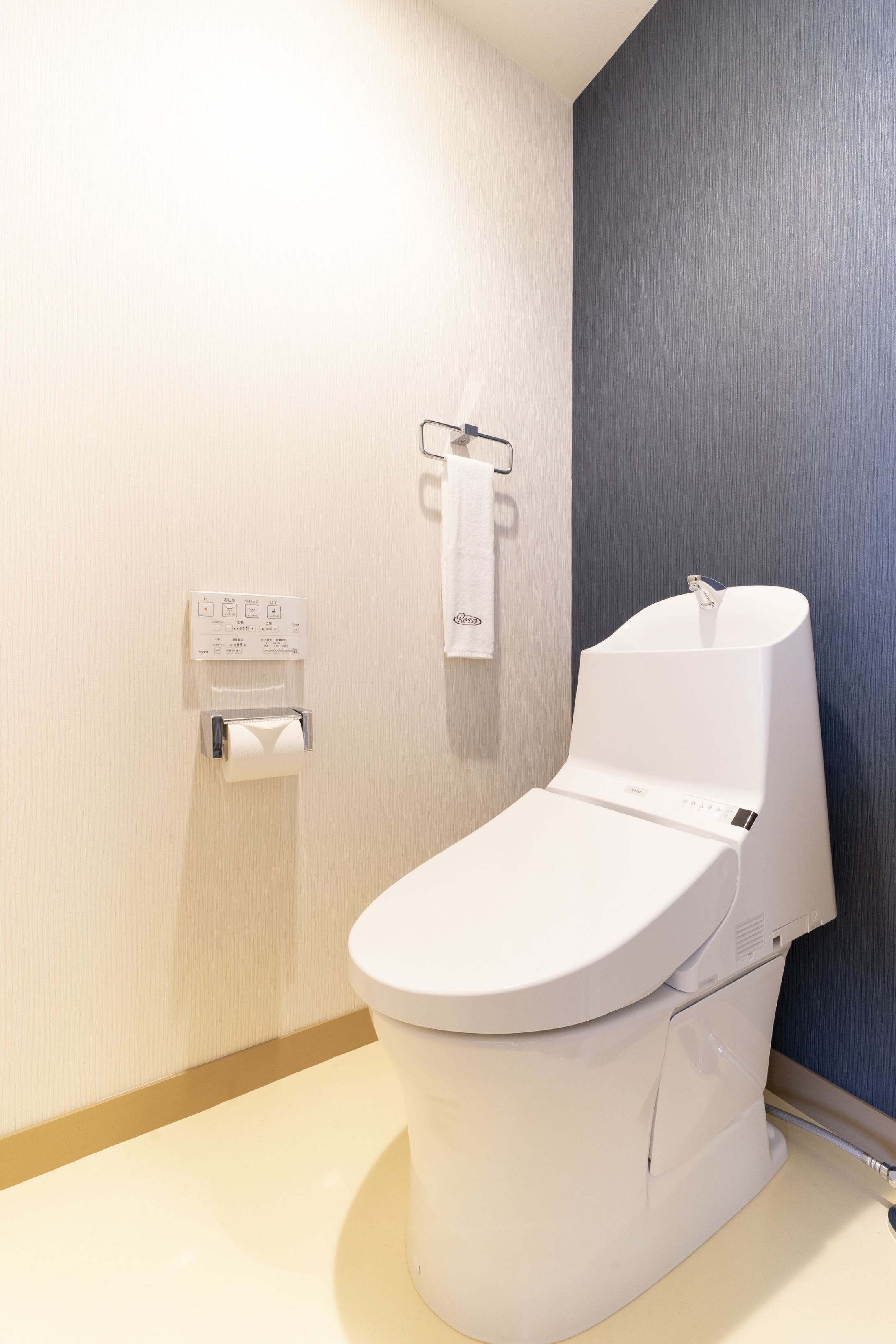 A modern bathroom with a white toilet, a paper towel dispenser, and a towel rack.