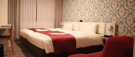 A hotel room with a large bed, a desk, and a red armchair.