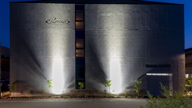 A large industrial building with a prominent 'Rosso' logo, featuring a central vertical window and multiple smaller windows. - Hotel Rosso Karuizawa (Karuizawa)