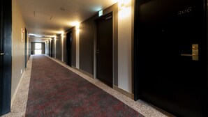 A hotel corridor with carpeted floors, doors, and wall-mounted light fixtures. - Hotel Rosso Karuizawa (Karuizawa)