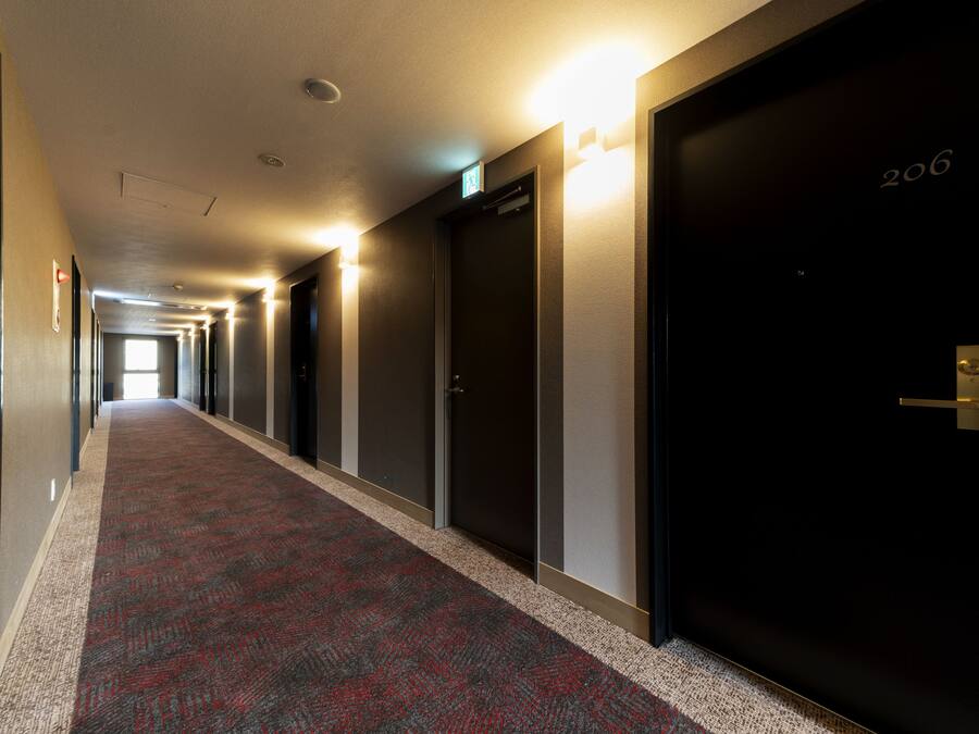 A hotel corridor with carpeted floors, doors, and wall-mounted light fixtures.