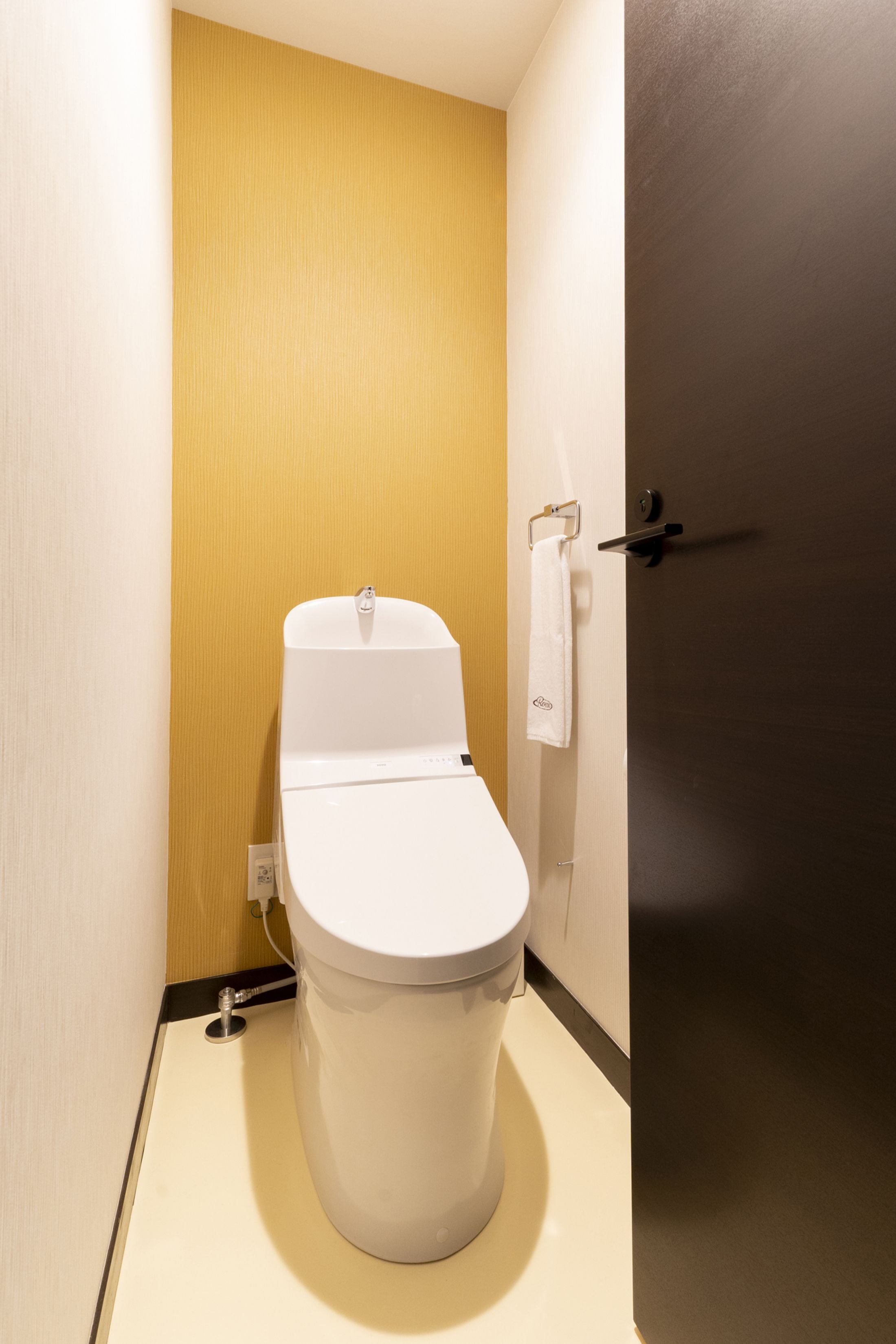 Ein kleines, modernes Badezimmer mit einer weißen Toilette, einem Handtuch auf einem Halter und einer Tür mit Griff.
