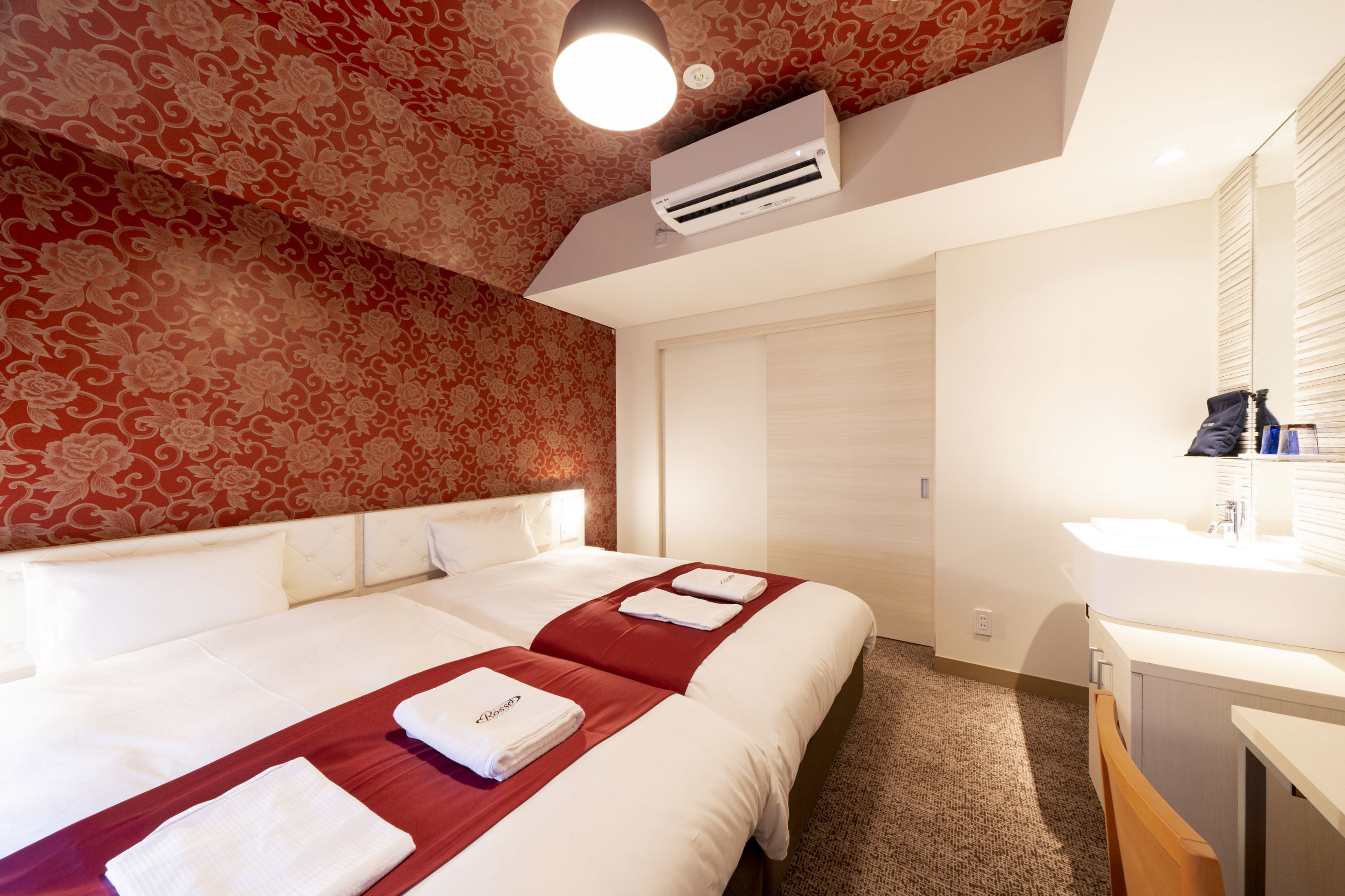 Habitación de hotel con dos camas, un espejo grande, un lavamanos y un techo con diseño.