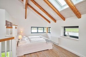 A bedroom with a wooden ceiling, a bed with white linens, a window with a view of greenery, and a small sailboat model on the windowsill. - Remise III - Holiday apartments Gut Oestergaard (Steinberg)