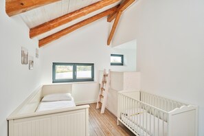 A room with a sloped ceiling, a crib, a window, and a ladder. - Remise III - Holiday apartments Gut Oestergaard (Steinberg)