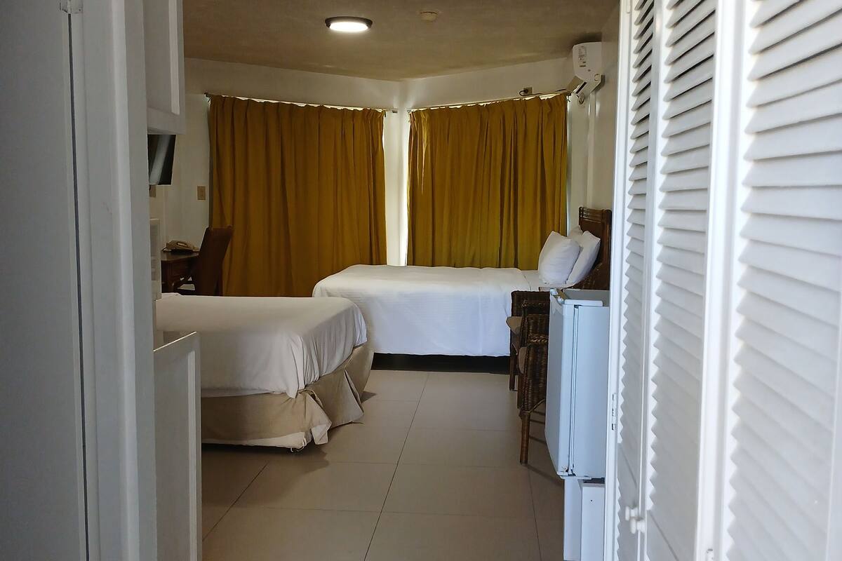 A hotel room with a bed, a desk, and a chair. There is a window with curtains, and a door leading to another room.