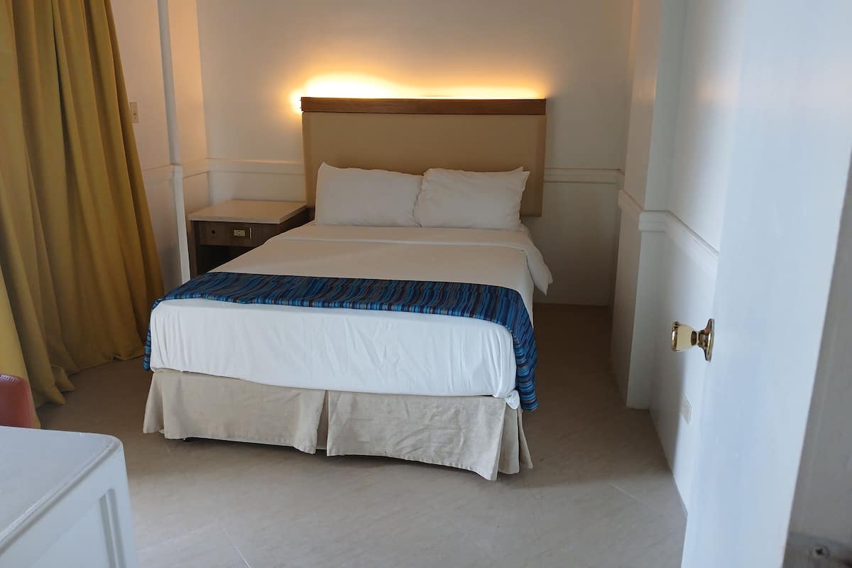 A hotel room with a bed, a nightstand, a lamp, and a door.