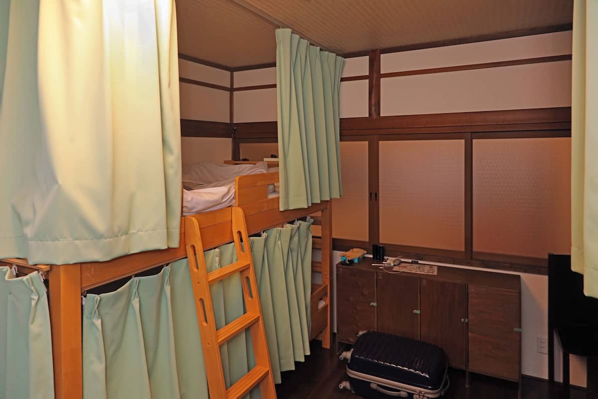 Een slaapkamer met een stapelbed, een ladder, een koffer en een houten kast.
