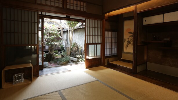 Ein traditioneller japanischer Raum mit Tatami-Böden, Schiebetüren und Blick auf einen Garten.