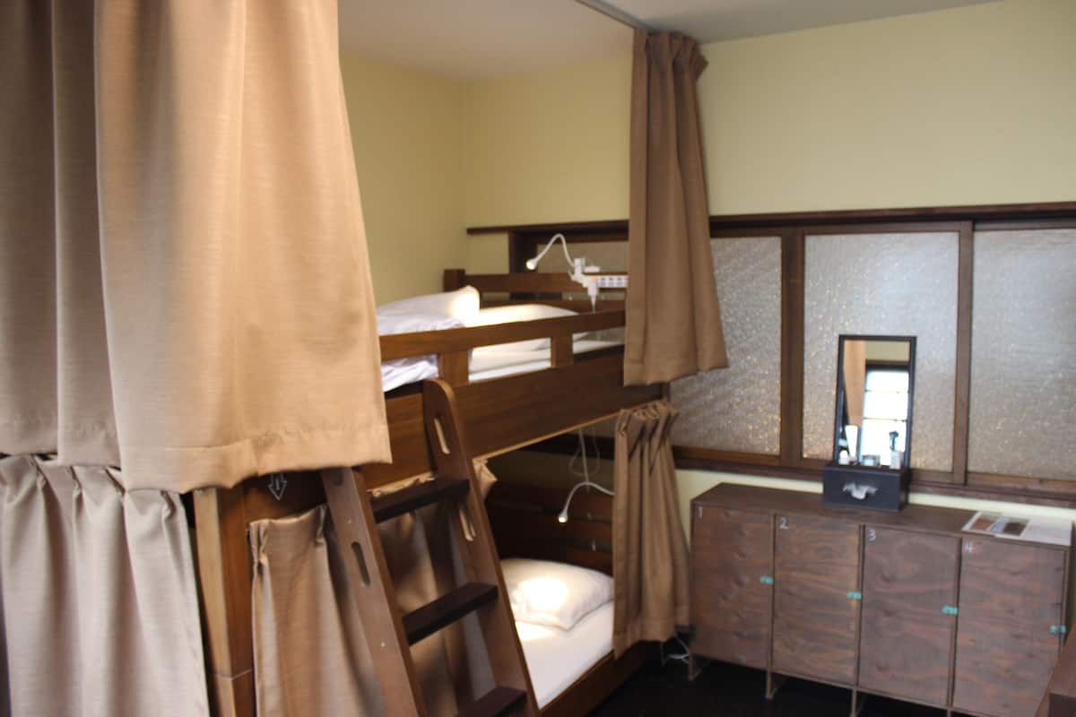 Een slaapkamer met een stapelbed, een houten dressoir en een spiegel.